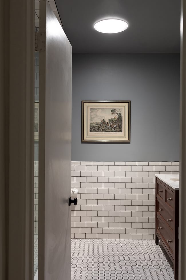 A Sun Tunnel skylight brightens a bathroom with white tile and grey walls