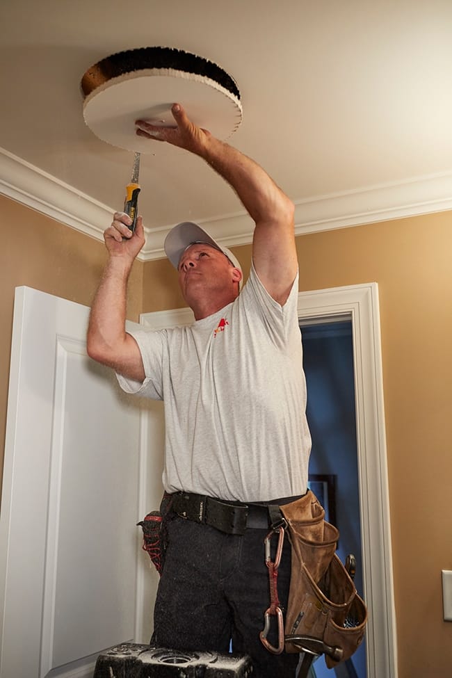 A man cutting a hole in the ceiling during a sun tunnel installation