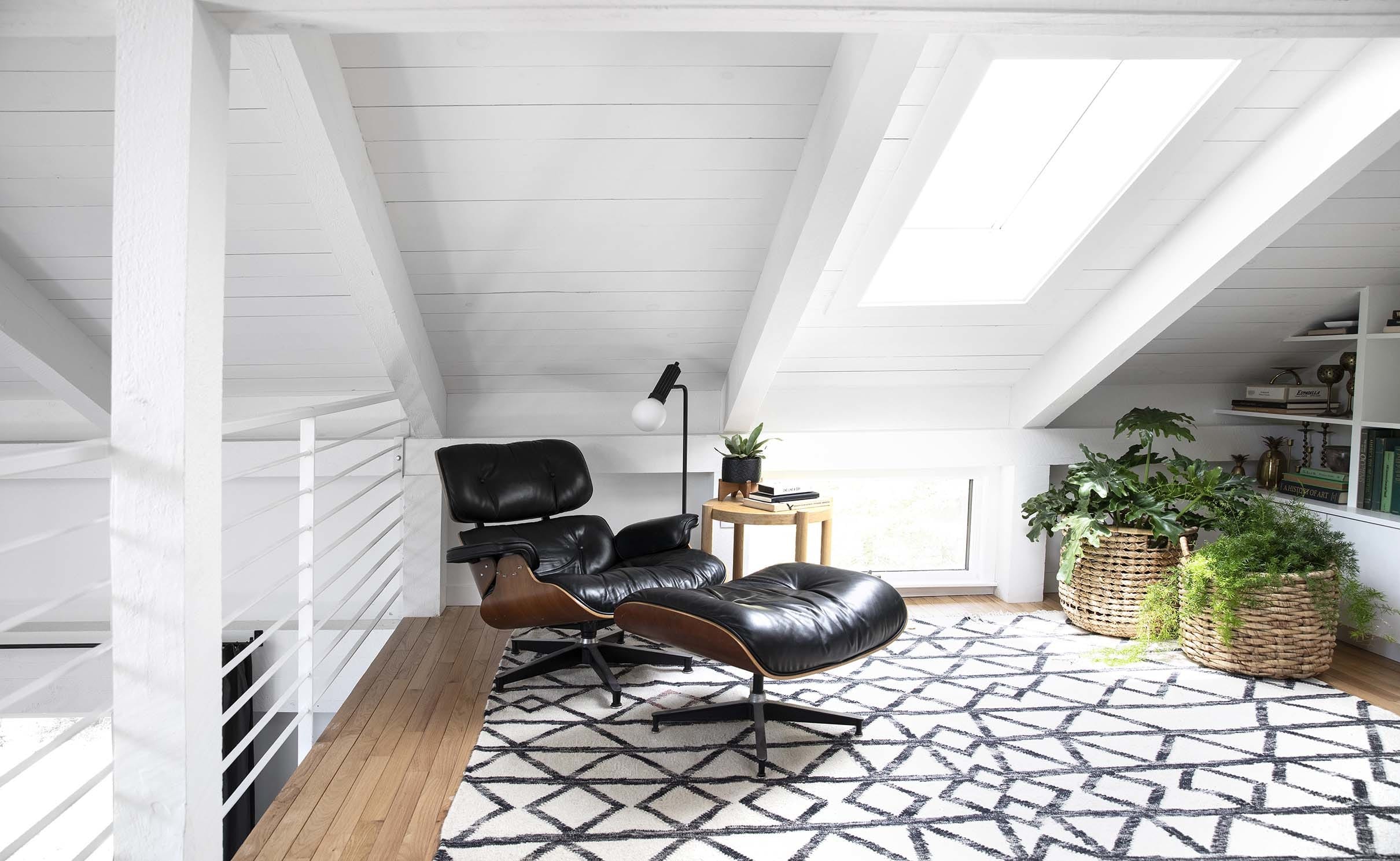 Black Eames chair under a skylight in a white wood clad room with built-in bookshelves and a geometric print rug
