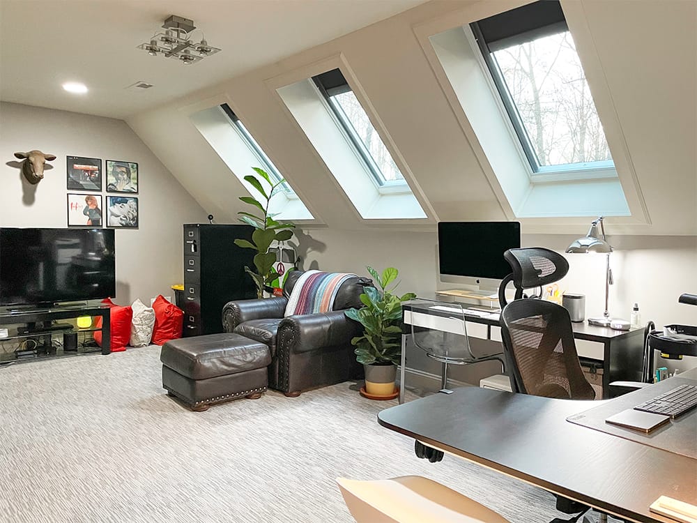 A home office with three skylights, leather furniture, record album art and a fiddle leaf fig.