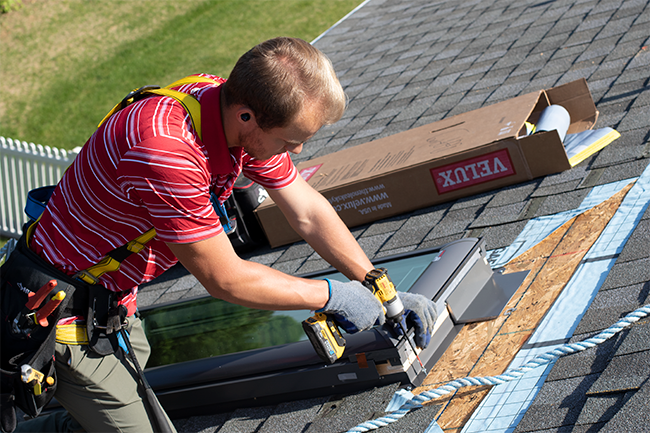 Man in red shirt screws a skylight to a roof