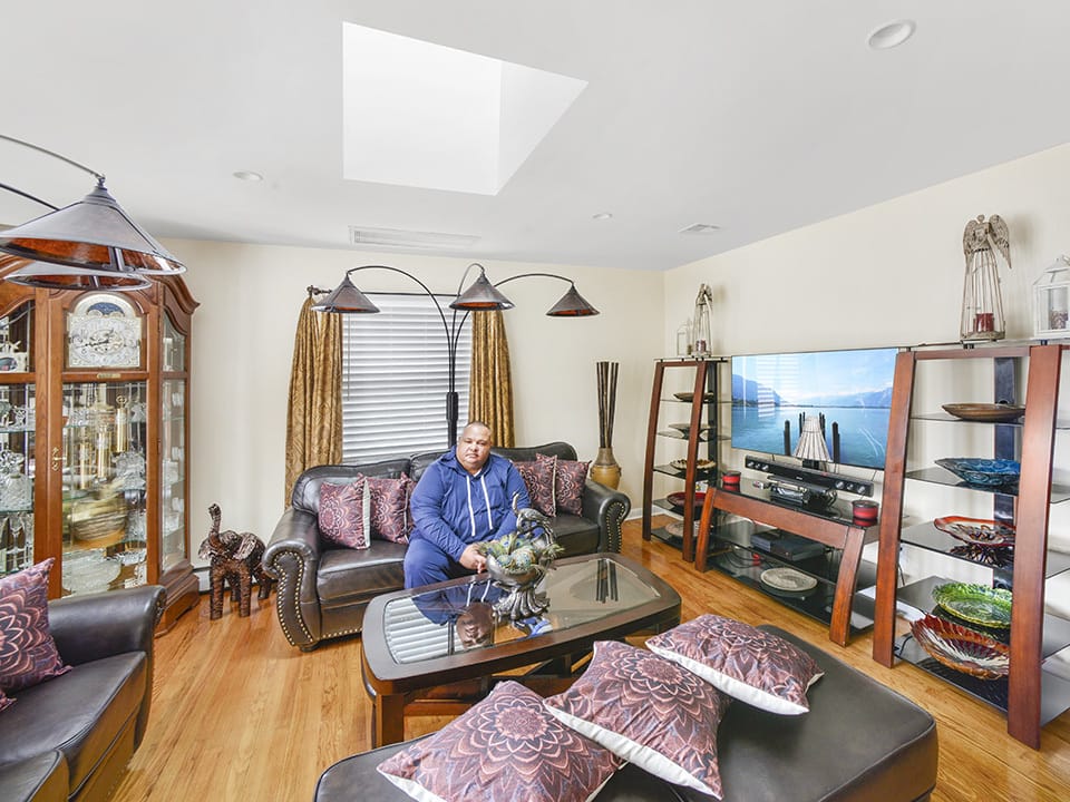 A man sits in his living room under a skylight.