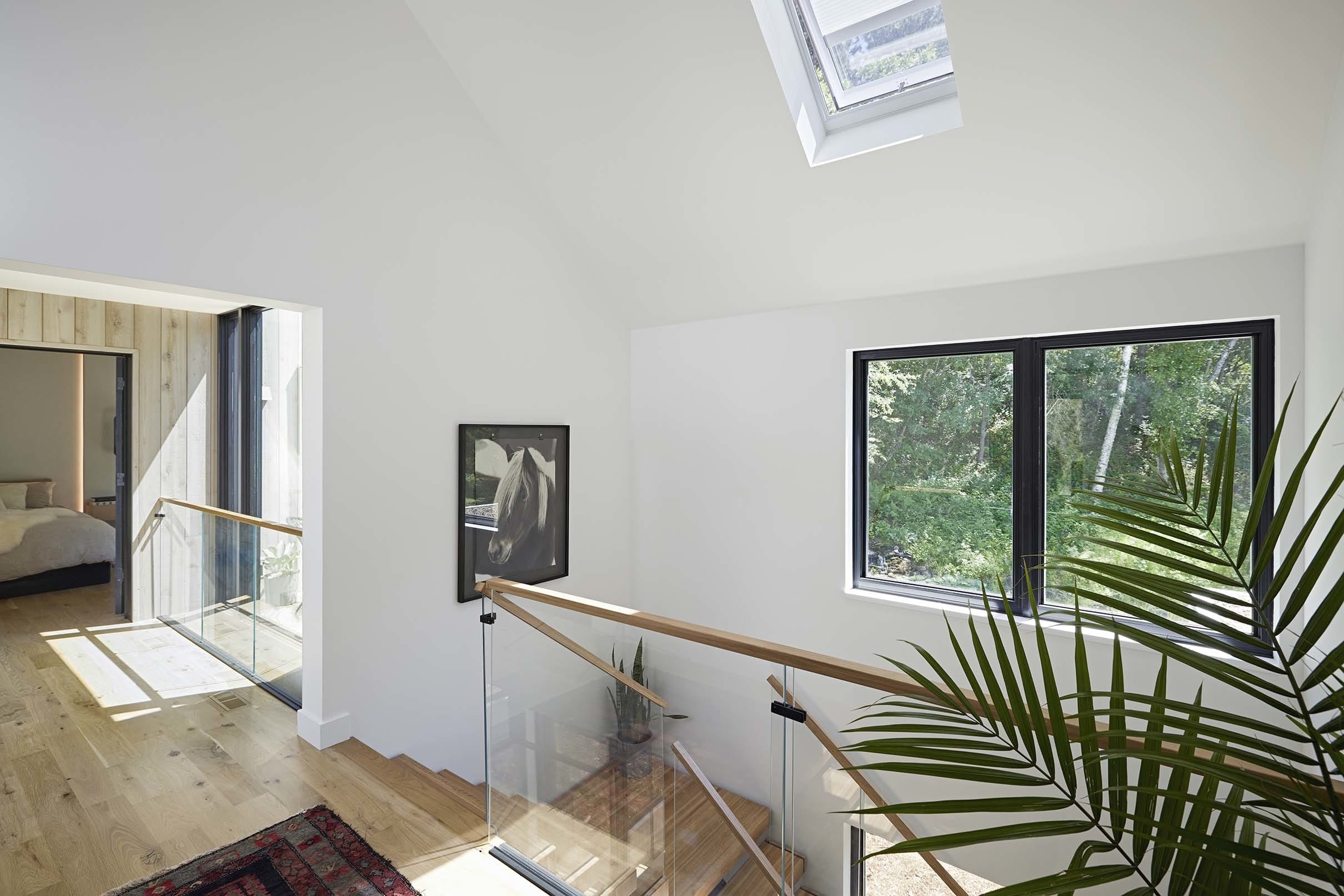 a stairwell brightened by a skylight white walls and blond wood floor
