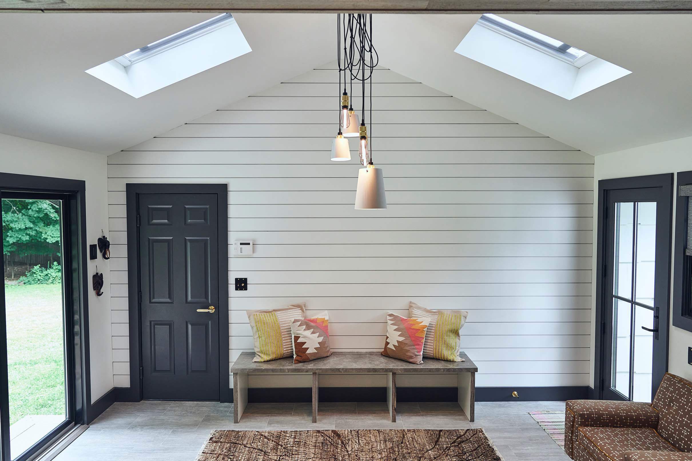 A sunroom with two skylights on either side of the roof ridge, a shiplap wall with a bench centered on it and pillows