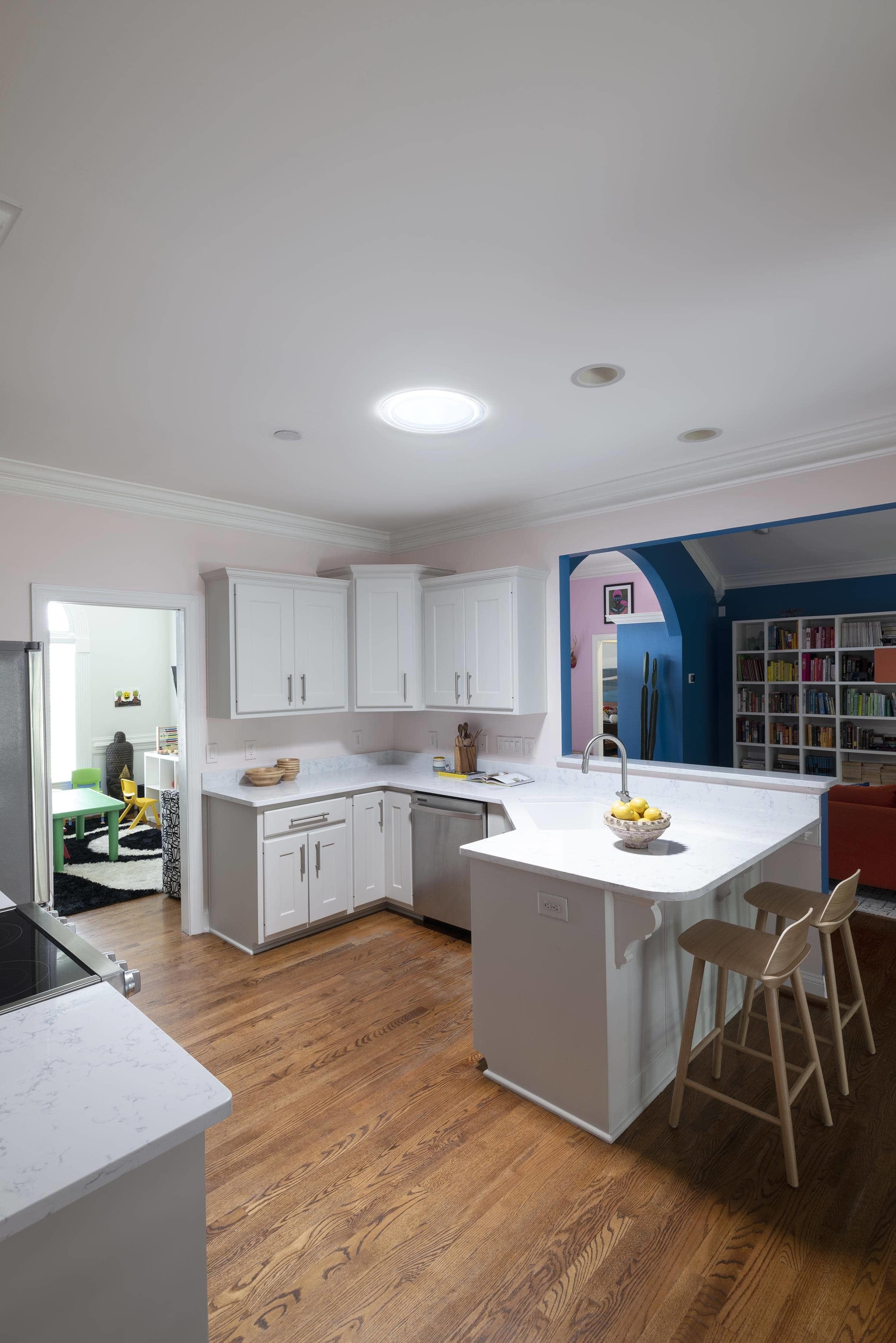kitchen with light pink walls, white cabinets and a Sun Tunnel skylight with a blue living room in the background