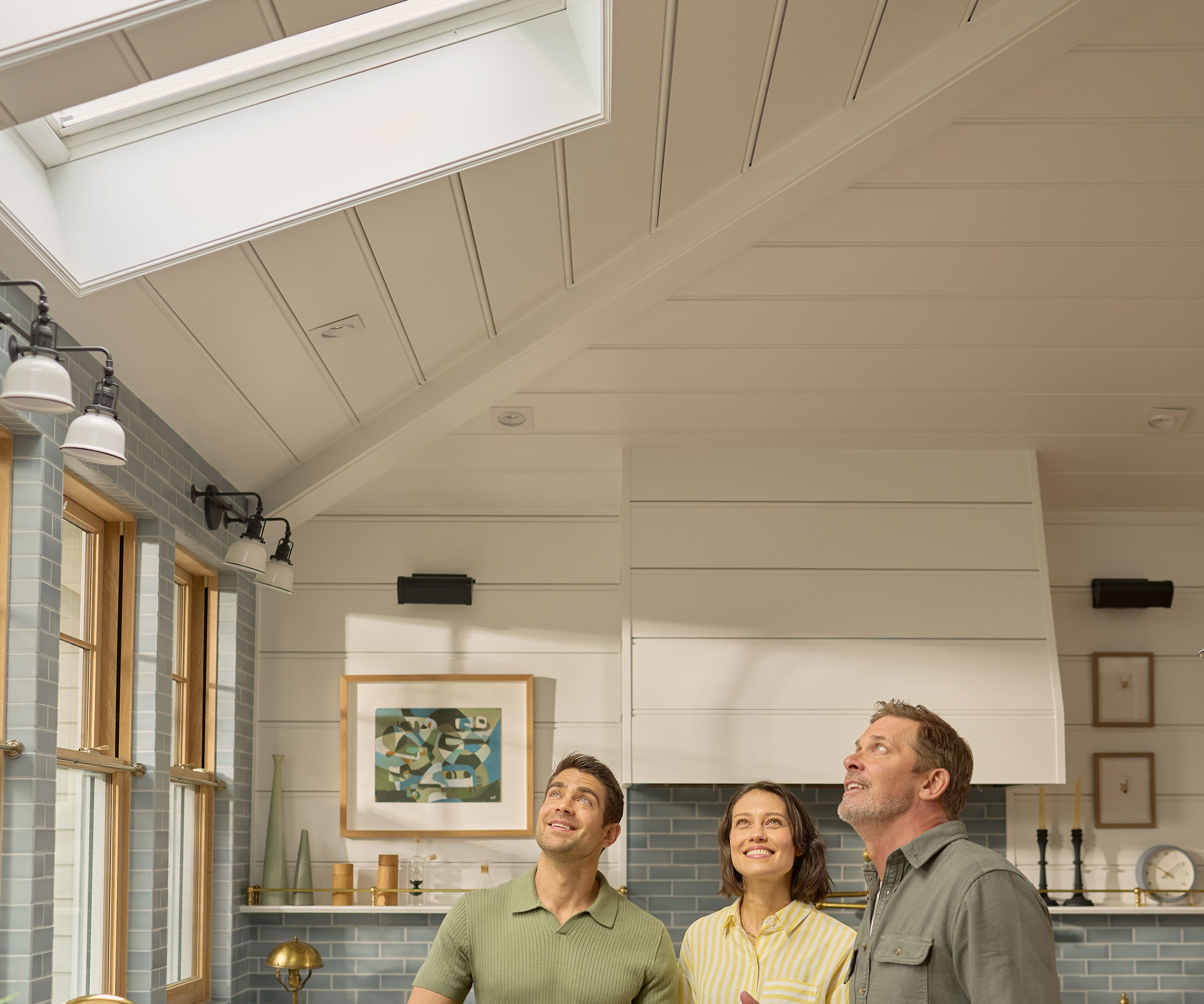 An installer explains the new skylights installed above them in their kitchen to a pair of homeowners.