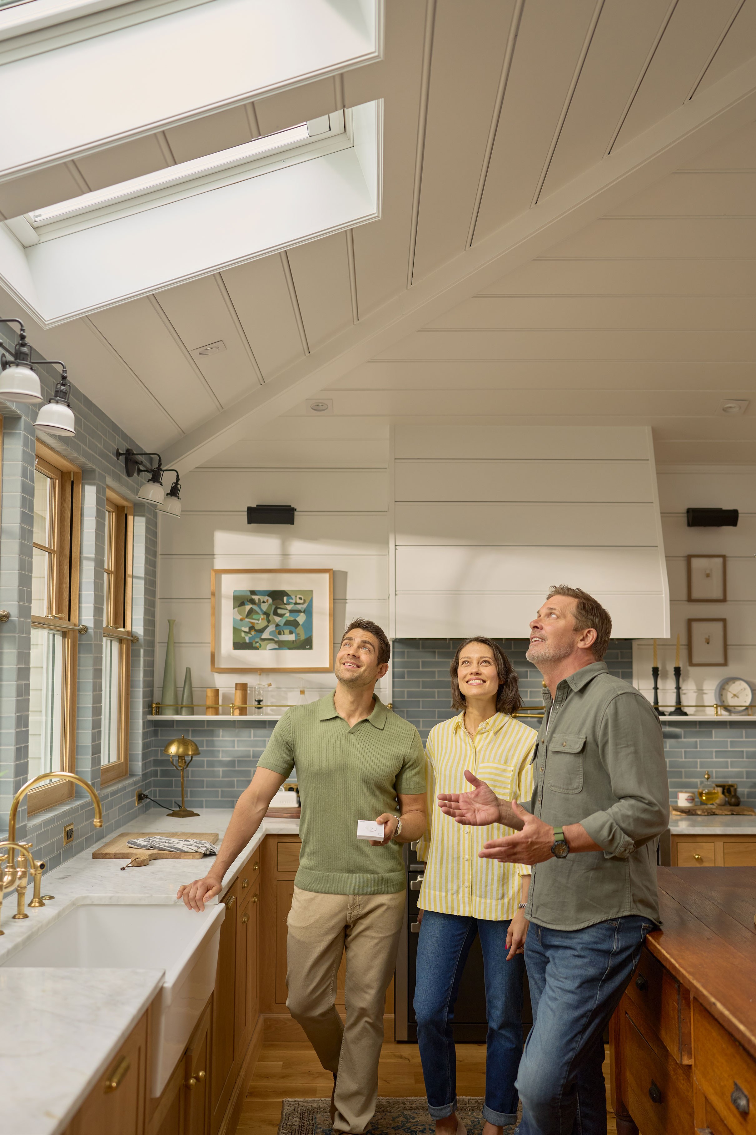 A skylight professional and two homeowners stand in a kitchen looking up at skylights. The professional is explaining the newly installe skylights while the homeowners are listening and smiling.