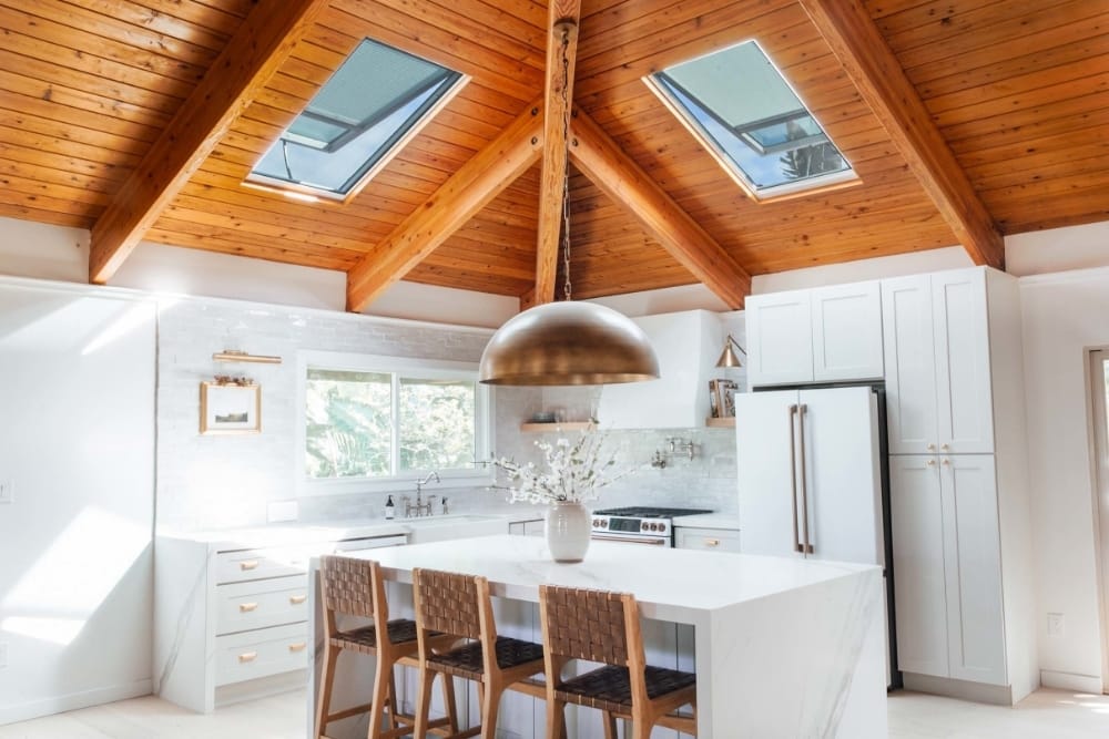White kitchen with natural wood ceiling two skylights and brass light fixtures